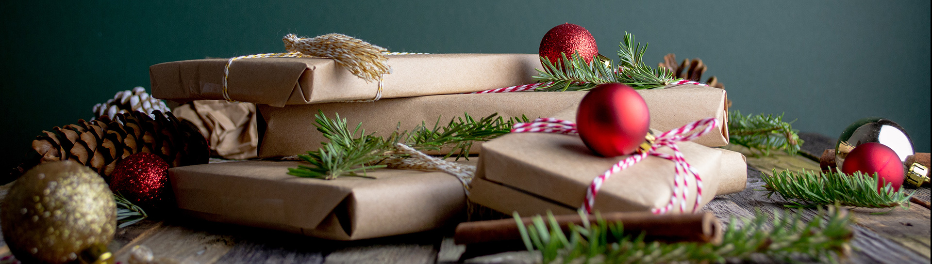 Collection of gifts wrapped in brown paper and natural materials with red and gold decorations on a dark green background
