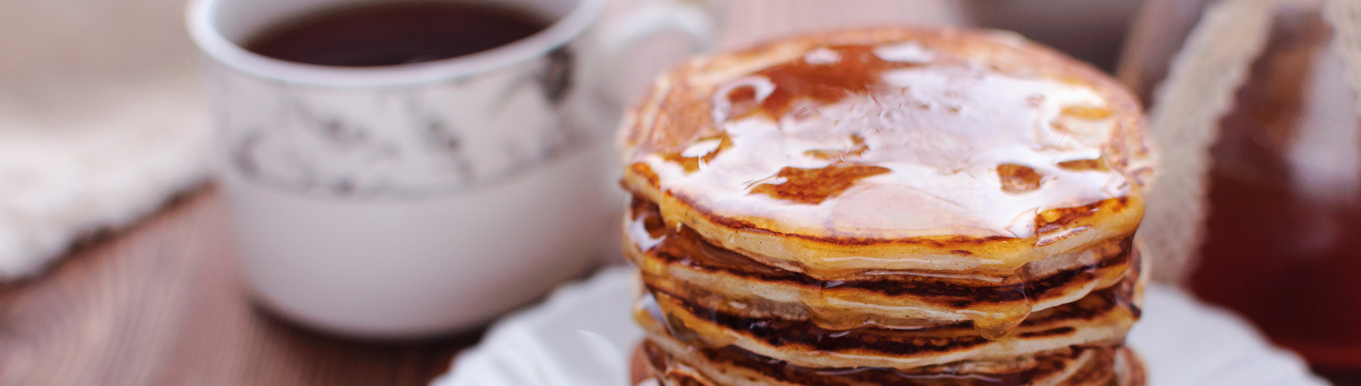 stack of pancakes with maple syrup dripping over them and a cup of coffee in the background